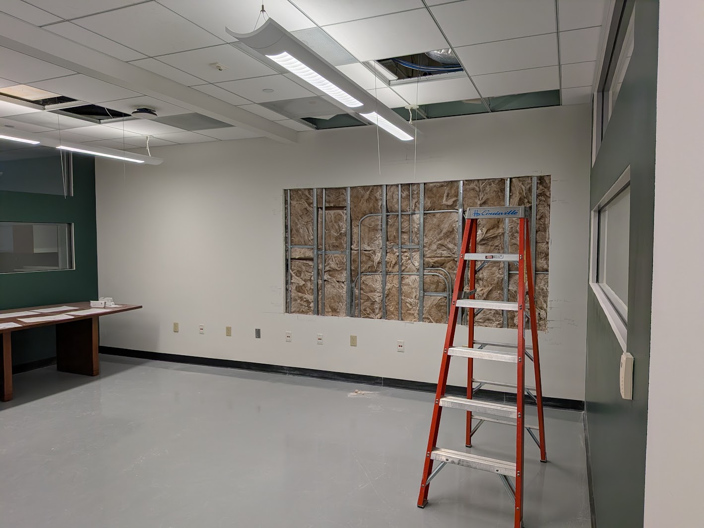 An instructional room during an active technology renovation with open ceilings, exposed wall framing, and a ladder
